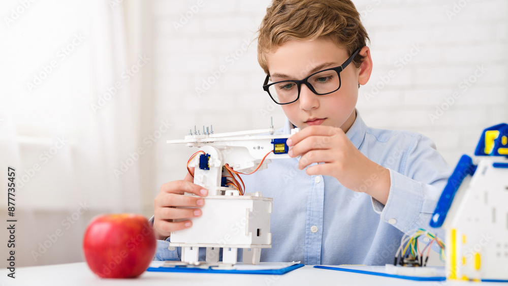 Aufkleber A young boy sits at a table, wearing glasses, and is deeply focused on assembling a robotics project. He holds a small component in his hand, carefully aligning it with the rest of the construction