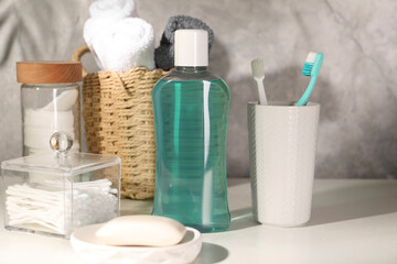 Bottle of mouthwash, toothbrushes and soap on light table in bathroom