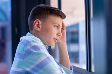 Thoughtful caucasian schoolboy looking out of window in classroom, with copy space