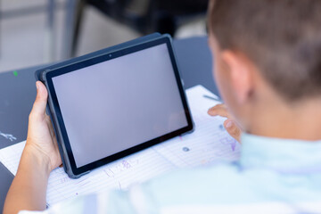 Caucasian schoolboy sitting at desk using tablet in class, with copy space on screen