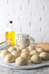 Raw dough balls, flour, rolling pin and oil on white marble table