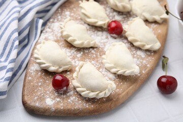Raw dumplings (varenyky) and fresh cherries on white tiled table, closeup