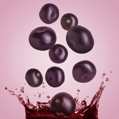 Acai berries falling into juice on pink background