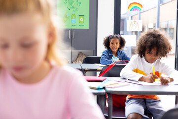 Happy diverse schoolchildren sitting at desks in school classroom