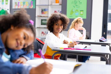 Happy diverse schoolchildren sitting at desks in school classroom