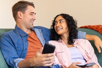 Smiling couple sitting on couch, holding smartphones and looking at each other