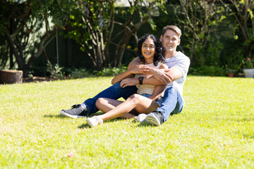 Sitting on grass, young couple hugging and smiling in sunny garden