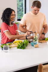 Preparing healthy smoothie, young couple blending fruits and vegetables in kitchen
