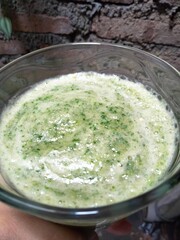 the hand holding a glass of smoothie that contain any vegetables with brick wall background.