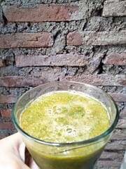 the hand holding a glass of smoothie that contain any vegetables with brick wall background.