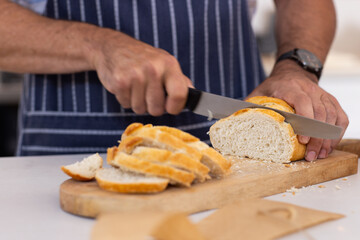 Slicing fresh bread on cutting board, person preparing meal in kitchen