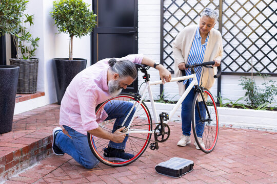 Fixing bicycle, senior man kneeling while woman holding bike in courtyard