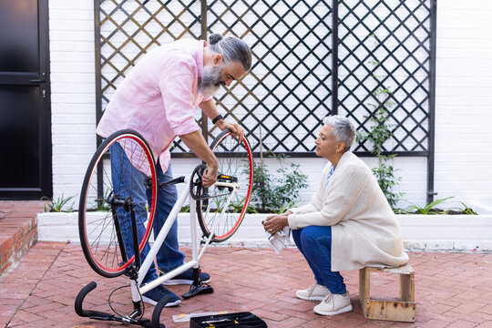 Repairing bicycle, senior man fixing bike while woman sitting and watching - Powered by Adobe
