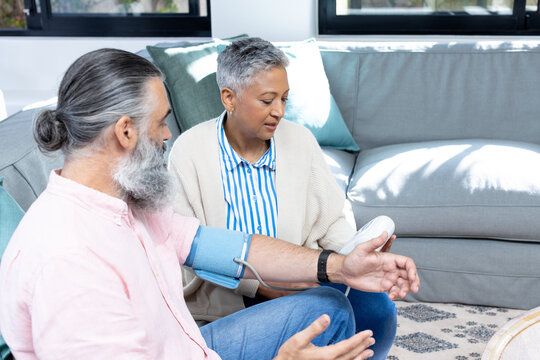 Checking blood pressure, senior couple sitting on couch in living room
