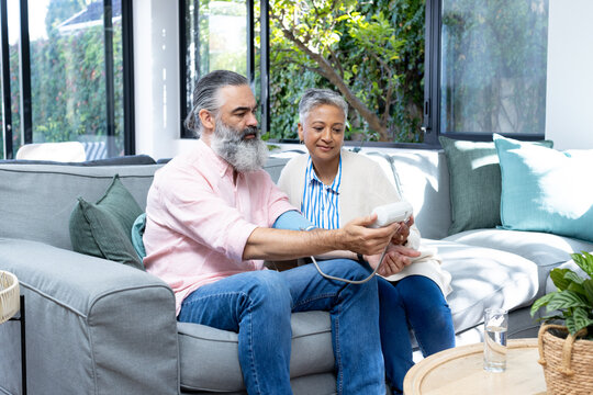 Senior couple checking blood pressure with monitor while sitting on couch