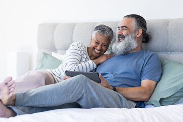 Relaxing on bed, senior couple smiling and using digital tablet together