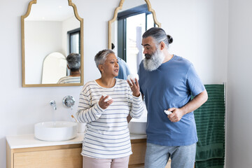Senior couple in bathroom applying skincare products and discussing routine