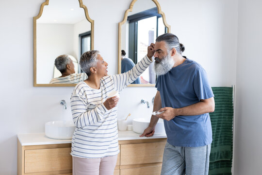Senior couple in bathroom, woman applying cream to man's face, smiling together - Powered by Adobe