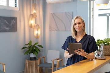 Smiling woman in medical clinic holding tablet, standing at reception desk, copy space