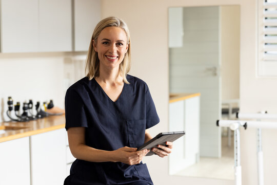 Holding tablet, woman in medical clinic smiling and wearing scrubs