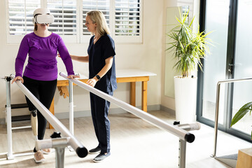 Woman in prosthetic leg walking using VR headset with therapist on parallel bars, copy space