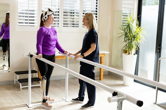Woman in prosthetic leg using VR headset with therapist on parallel bars - Powered by Adobe