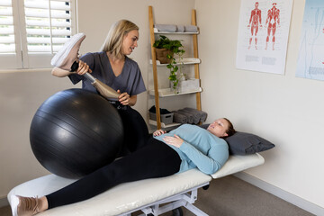 Physical therapist assisting woman with prosthetic leg using exercise ball in clinic