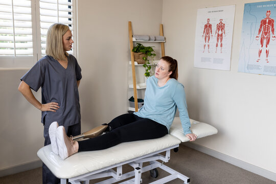 Physical therapist talking to woman with prosthetic leg sitting on examination table