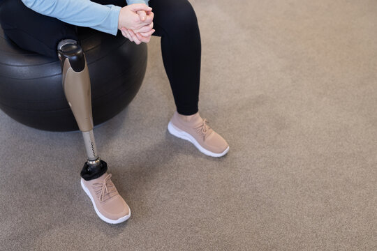 Sitting on exercise ball, person with prosthetic leg wearing athletic shoes, copy space