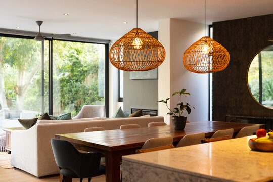 Modern dining area with wooden table and wicker pendant lights in cozy home, copy space