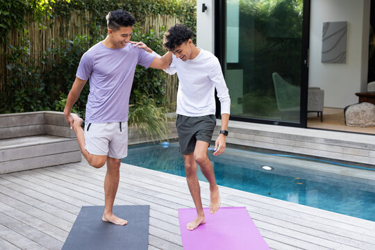 Stretching together on yoga mats, male gay couple enjoying outdoor exercise by pool - Powered by Adobe