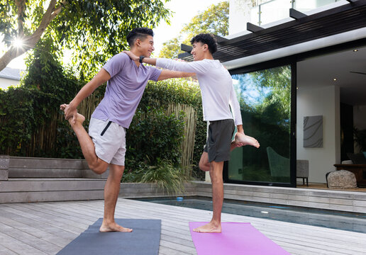 Practicing yoga, male gay couple balancing on one leg on yoga mats outdoors