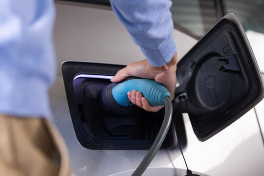 Charging electric car, person plugging in charger at home station