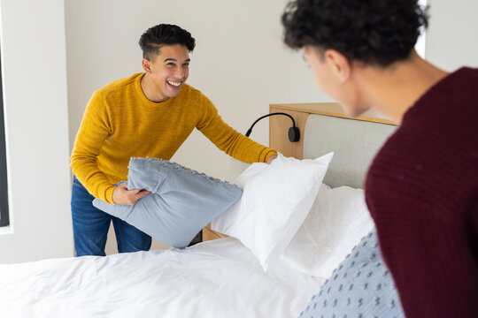 Making bed together, smiling male gay couple arranging pillows in bedroom