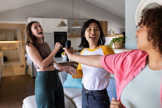 Singing karaoke, three women friends enjoying time together in living room