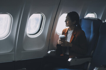 Young Asian female tourist traveling alone on a plane is drinking hot coffee and looking out the window.