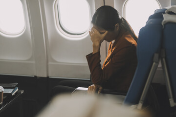 Stressed and serious young asian businesswoman remote working on the plane, suffering from headache...