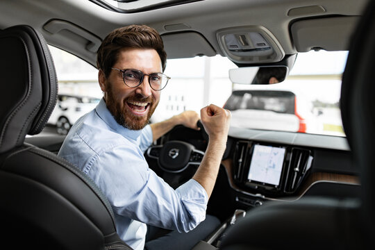 Person joyfully sits inside a vehicle at dealership. Happy businessman celebrates new car purchase. Cheerful moment of acquiring automobile. - Powered by Adobe