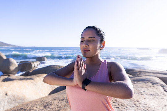 Practicing yoga, woman meditating with hands in prayer position by ocean