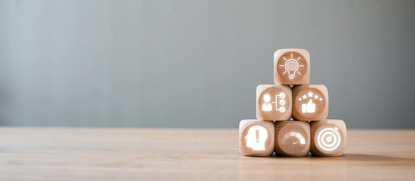 Wooden blocks with icons symbolizing skills, knowledge, and performance stacked in a pyramid on a wooden table, illustrating the concept of competence.