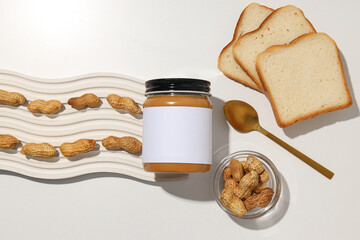 Peanut paste in a glass jar with a spoon, on a light background.
