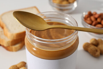 Peanut paste in a glass jar with a spoon, on a light background.