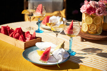 A bright summer garden setting in a yellow palette, with a yellow tablecloth, a vase of lemons with...