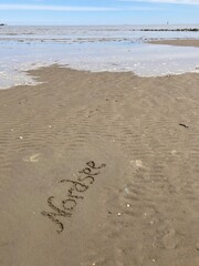 Schriftzug Nordsee im niedersächsischen Wattenmeer vor Cuxhaven mit steigender Flut