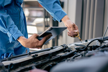 Automotive mechanic repairman using tablet and pulling dipstick to checking engine oil level engine in the engine room, check the mileage of the car, oil change, auto maintenance service concept.