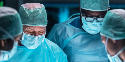 Team of medical doctors performs surgical operation in modern operating room using high-tech...