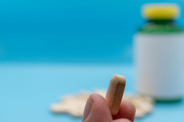 Hand taking a vitamin or medicine tablet, bottle with blank rx out of focus on background pharmacy and health concept