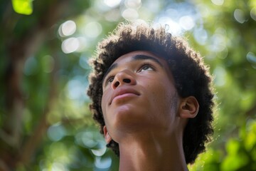 A young man with curly hair looks up with a puzzled expression, surrounded by vibrant green foliage