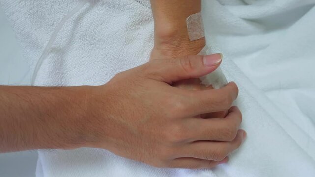 Close up hand of a son touching elderly mom patient&rsquo;s hand to comfort her in hospital ward.