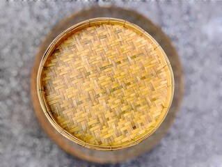 In the picture is a tray or wicker material made from brown bamboo in the shape of a circle with a thick edge. The inside is woven into various patterns that are reminiscent of ancient patterns and ha